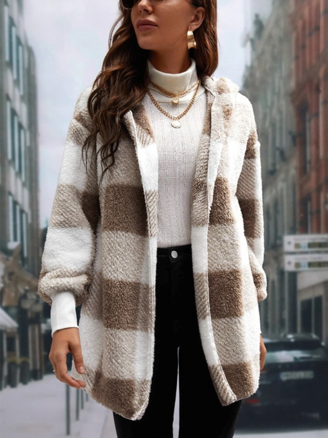 Woman wearing a stylish plaid long sleeve hooded coat over a white sweater, paired with black pants, walking in an urban setting.